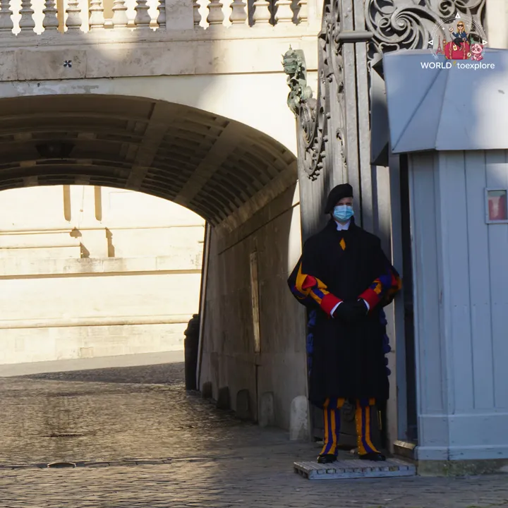 A Swiss Guard in the blue, red and yellow striped uniform, beside one of the gates into the Vatican