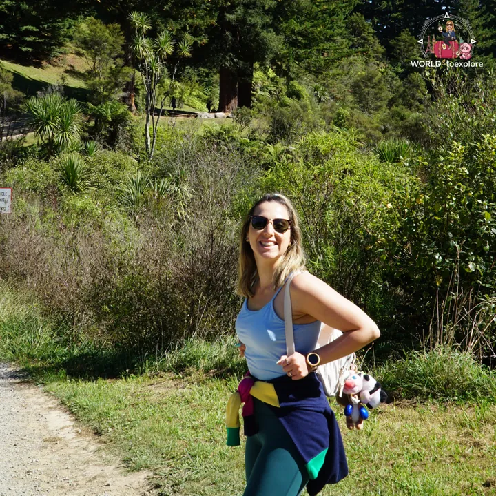 The author smiling on the Blue Spring trail, wearing sunglasses and a blue top, with tree ferns and native vegetation behind her