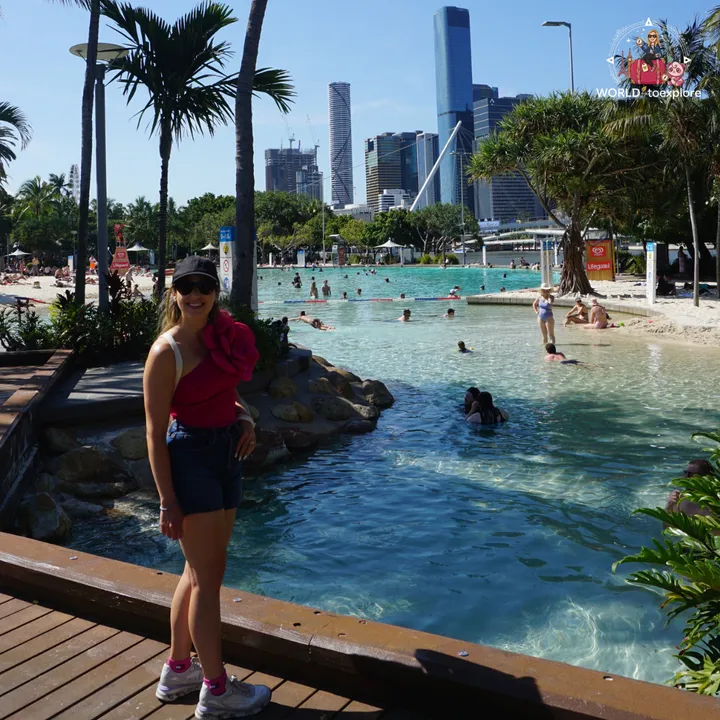 Streets Beach during the day, surrounded by palm trees and sand, with the Brisbane skyline in the background