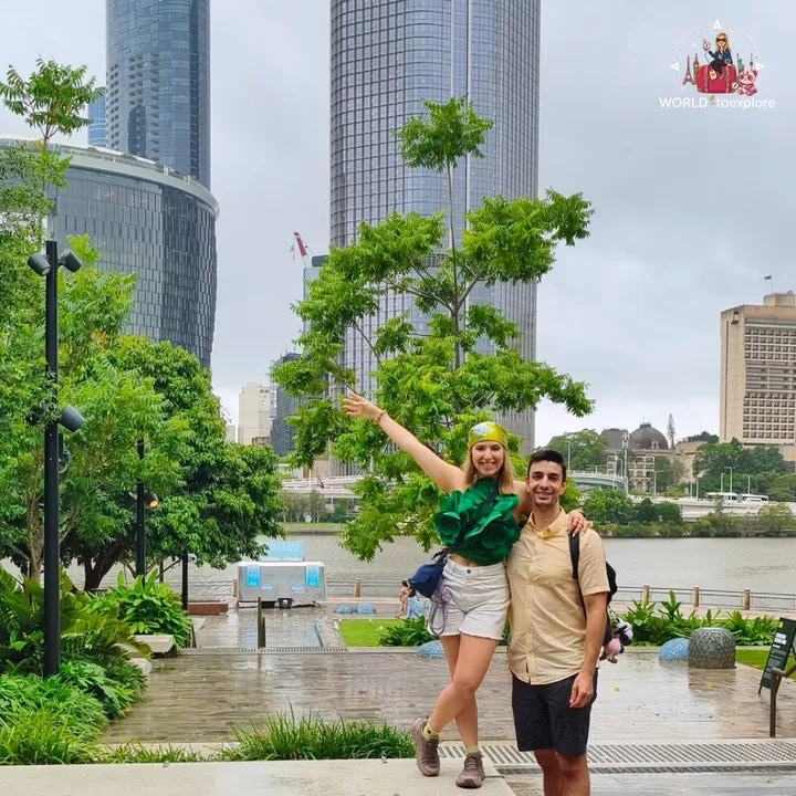 A green, tree-lined area of South Bank by the river, with the towers of The Star in the background on a cloudy day