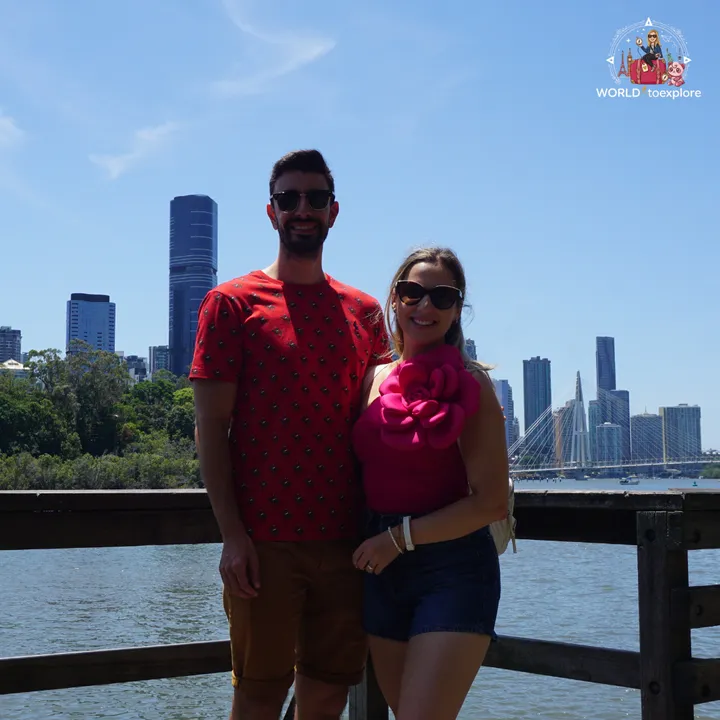 On a wooden boardwalk over the Brisbane River, with the city skyline and the Neville Bonner Bridge in the background