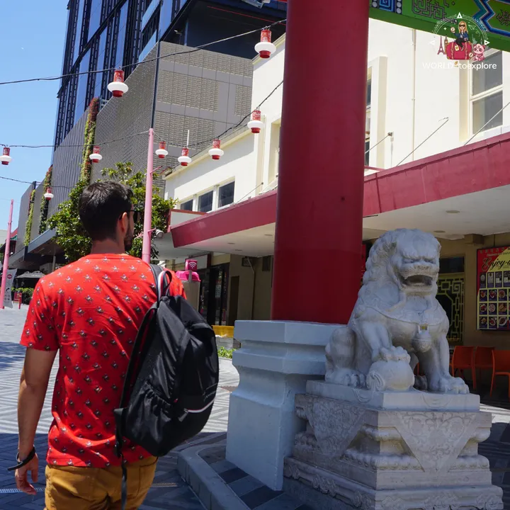 Walking past a stone guardian lion on a red pillar, in Chinatown