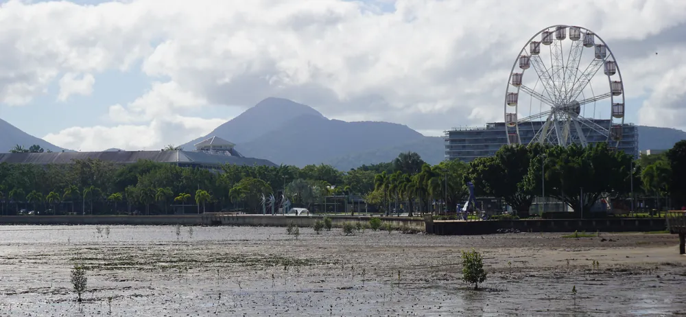 The Cairns waterfront at low tide, with the mudflats, the Reef Eye ferris wheel and the mountains behind