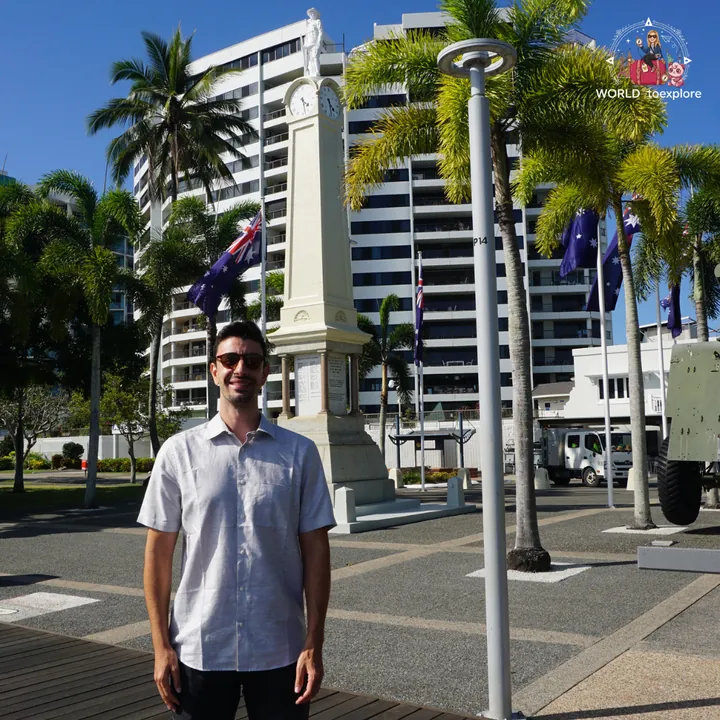By a monument on the Cairns Esplanade, flanked by palm trees and flags