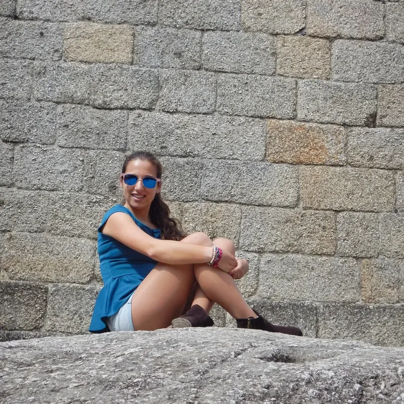 Woman in a blue top and sunglasses sitting on a rock against the castle's granite wall
