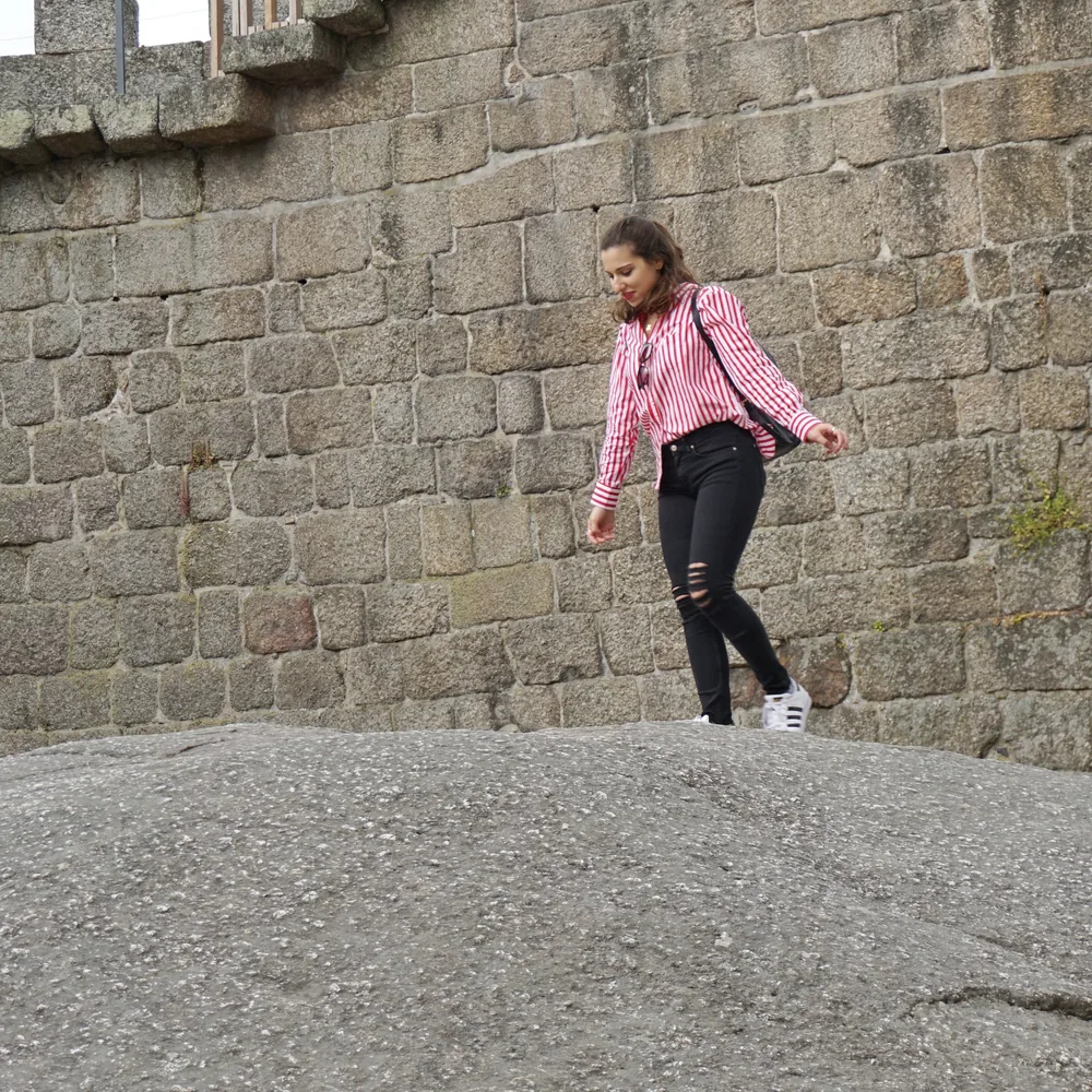Woman in a striped shirt climbing down a granite boulder beside the castle wall