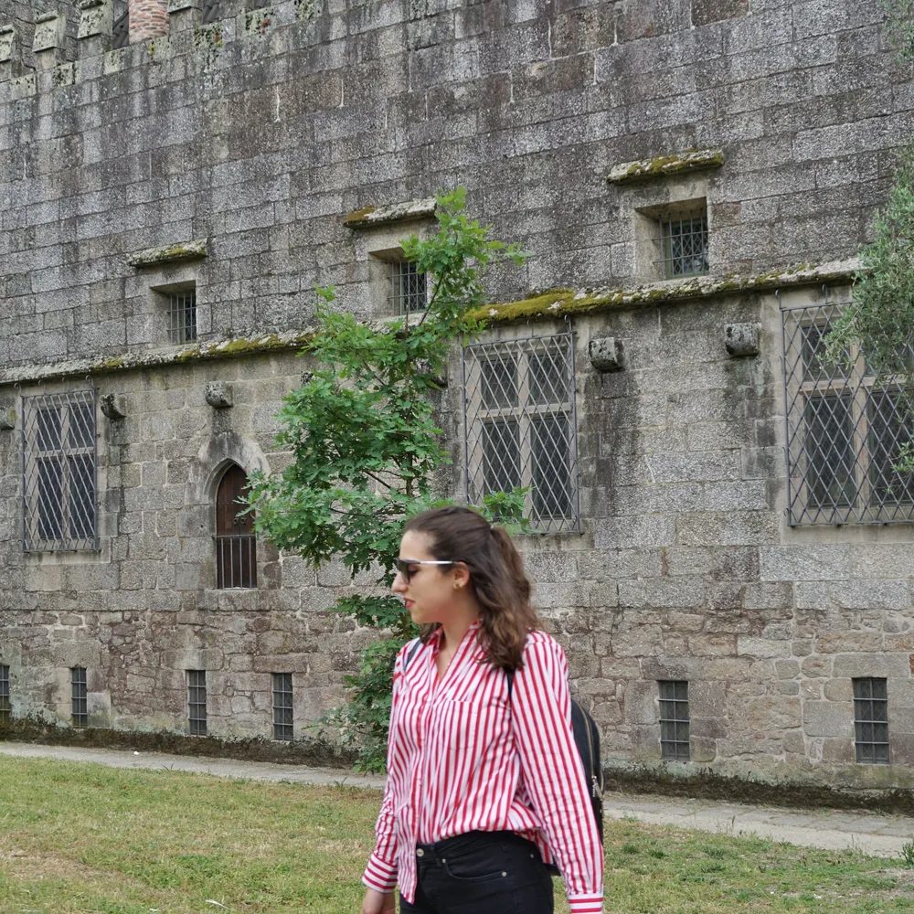 Woman in a striped shirt walking past the stone facade of the Paço dos Duques palace, with its barred gothic windows