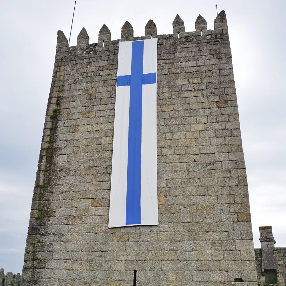 Looking up at one of the castle's towers, with a large blue cross banner draped between the battlements