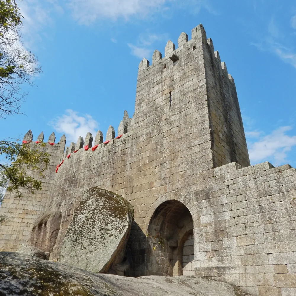 The keep and entrance archway seen from below, battlements lined with red flags against a blue sky