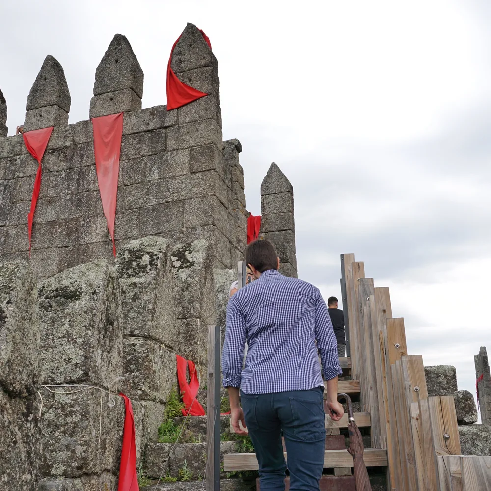 A man climbs a wooden staircase built over the castle walls, decorated with red flags