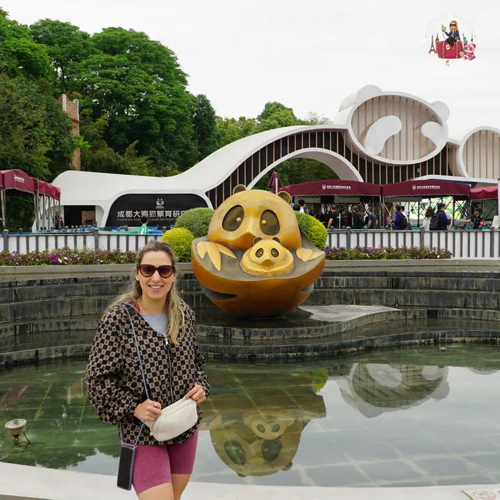 Cristina smiling by the entrance fountain of the Chengdu Research Base, with a golden statue of a panda and its cub in the background