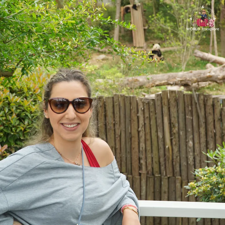 Cristina sitting down, with a giant panda visible in the background, next to a wooden fence