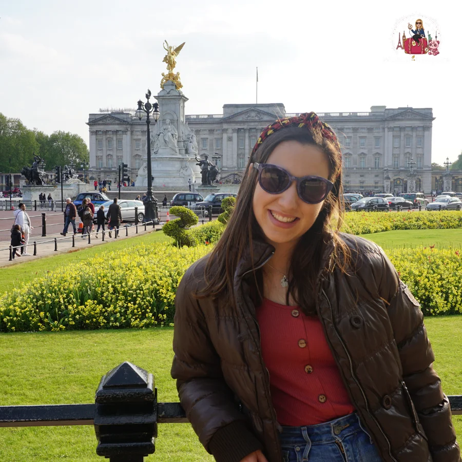 In front of Buckingham Palace in London, with the Victoria Memorial and its gilded figure behind and beds of yellow flowers in the foreground
