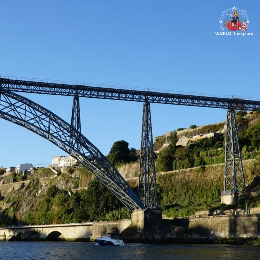 The iron Maria Pia Bridge seen from the River Douro, with the vegetation of the hillside and a boat passing underneath