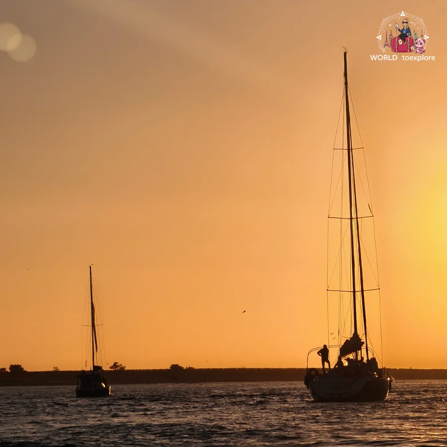 A sailing boat silhouetted against the orange sunset sky over the Atlantic Ocean, near the mouth of the Douro