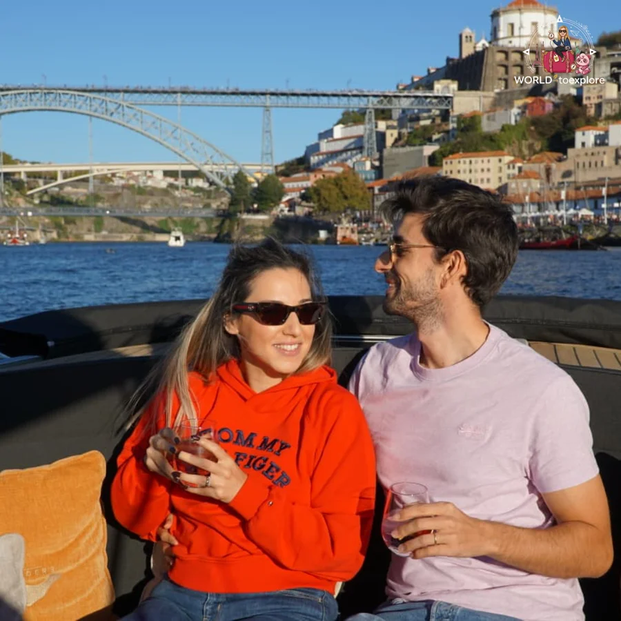 Cristina and her husband looking at each other aboard the Wondy, glass in hand, with the Luís I Bridge behind them