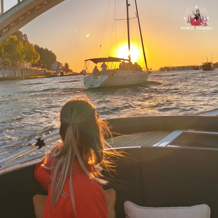 Cristina seen from behind watching the sunset over the River Douro, with a sailing boat ahead and golden light reflected on the water