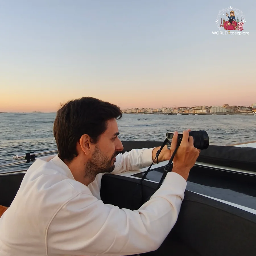 António, in a white sweater, photographing the horizon with a camera aboard the Wondy, with the Foz coastline behind him