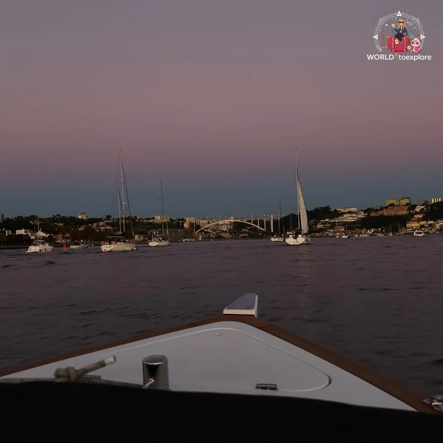 The bow of the Wondy at dusk, with sailing boats and the Arrábida Bridge in the background, on the River Douro at twilight