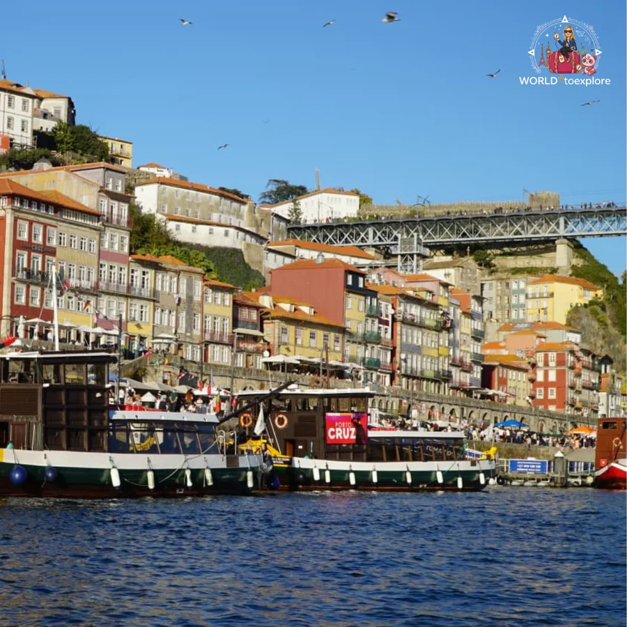 The colourful houses of the Ribeira in Porto seen from the River Douro, with the Luís I Bridge behind and tourist boats at the quay