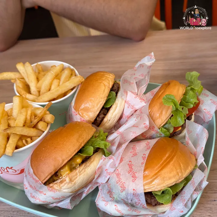 Four Betty's Burgers wrapped in branded paper, next to two cups of fries