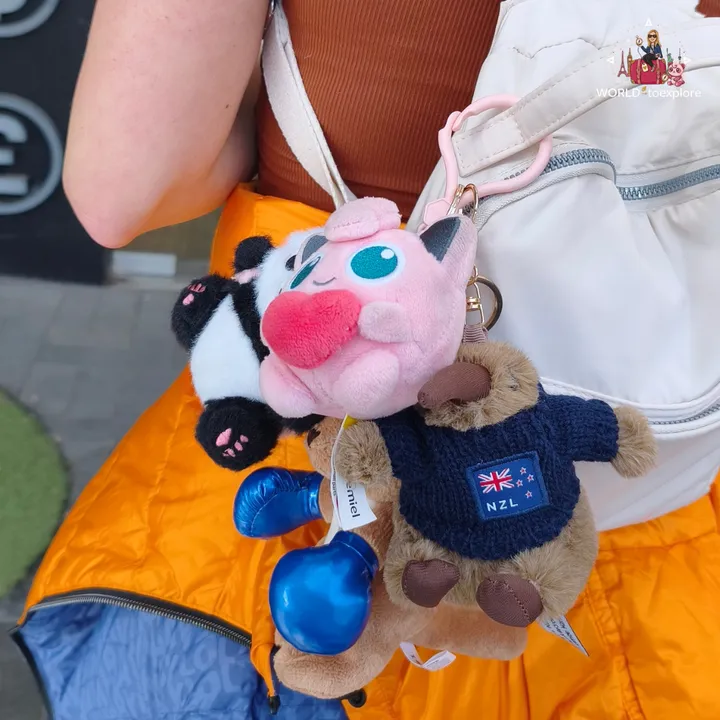 Plush keychains hanging from a backpack, including a kangaroo wearing a New Zealand jumper and a pink cartoon character