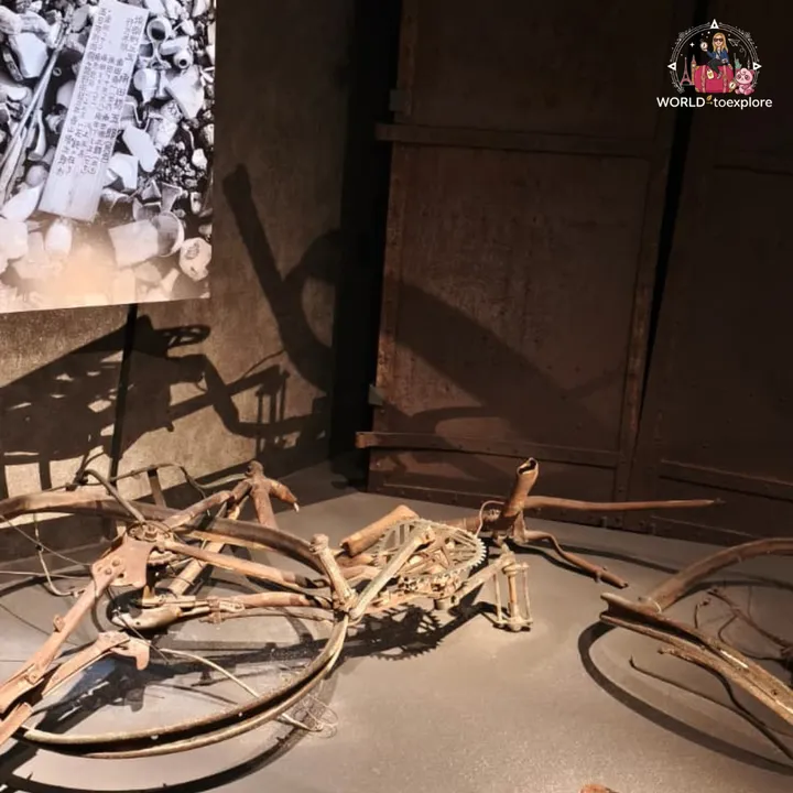 A bicycle twisted and burnt by the explosion, displayed in front of a photograph of the rubble