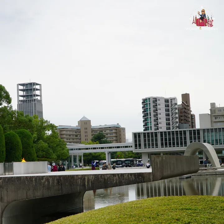 The Peace Flame burning beside the park's pond, with the stone arch of the cenotaph on the right and the raised museum building in the background