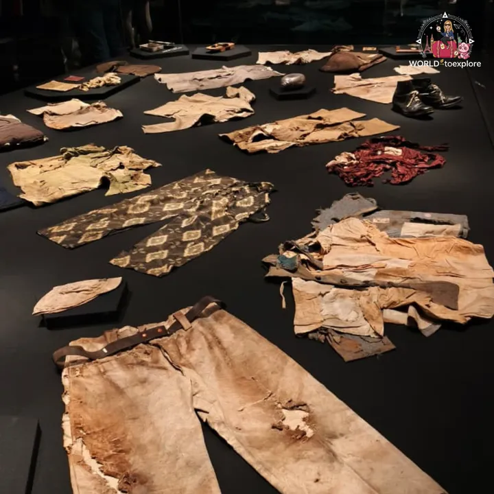 Torn and burnt pieces of clothing on display, including trousers with a belt, traditional patterned trousers and a pair of boots
