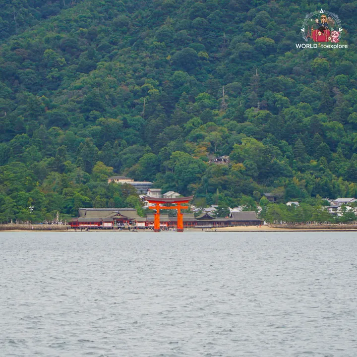 Itsukushima Shrine and the great red torii seen from the sea, with the wooded slopes of Mount Misen behind