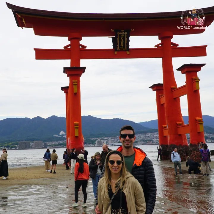 The two of us beneath the great torii up close, with its gold plaque of Japanese characters and the supporting pillars