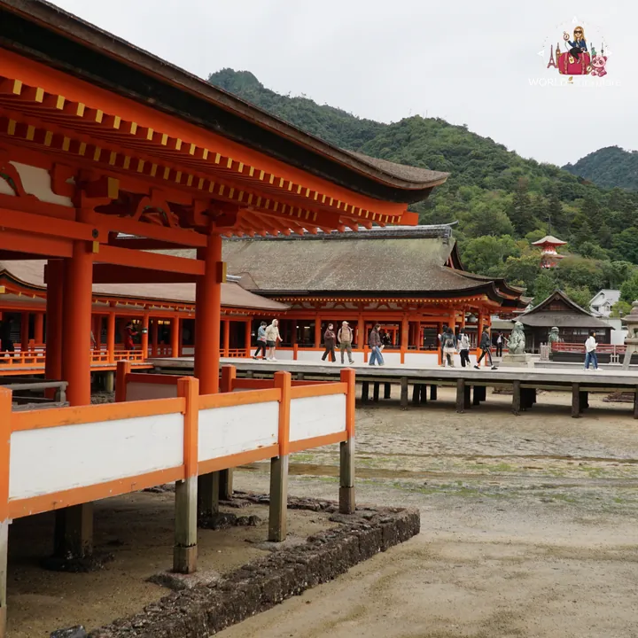 The shrine’s red-pillared corridors resting on stilts, with the tide out and visitors walking along the boardwalk