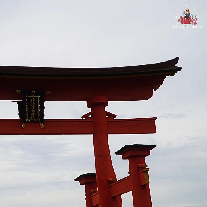 Close-up of the great red torii seen from below, with its gold plaque of Japanese characters and curved beam against the sky