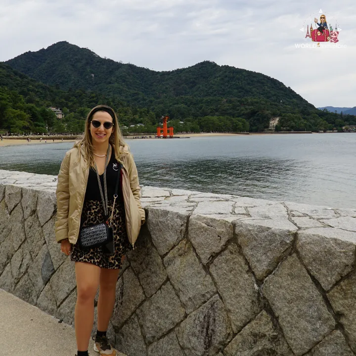 By the stone wall along the Miyajima seafront, with the beach, the great torii in the distance and the island’s wooded hills behind