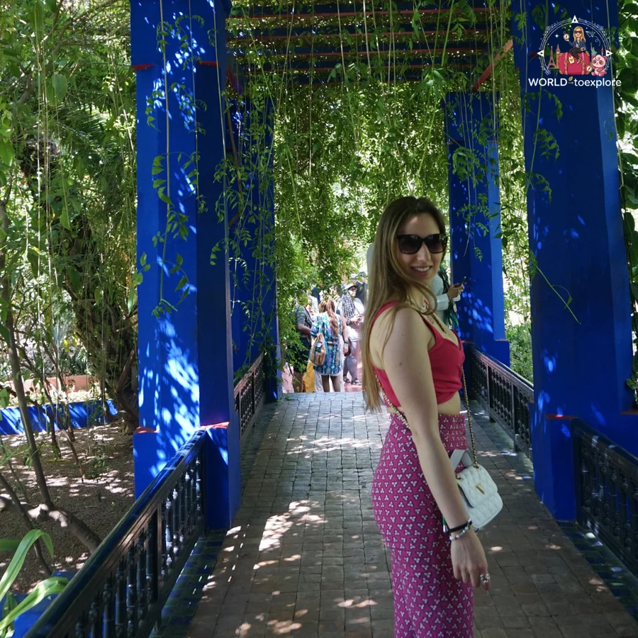 Woman looking back on a blue pergola covered in climbing plants, with the brick path ahead