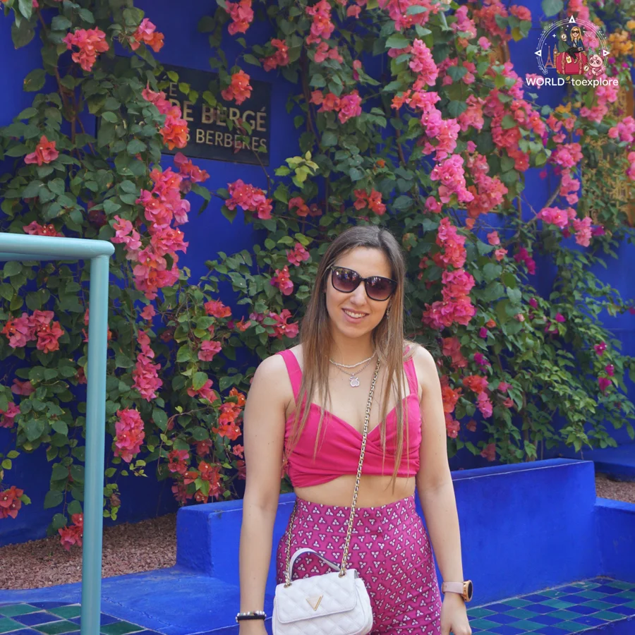 Smiling woman in front of a blue wall covered in pink bougainvillea, with the museum sign behind
