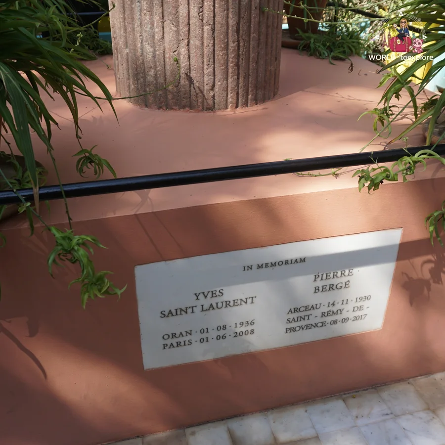 'In memoriam' plaque to Yves Saint Laurent and Pierre Bergé, with their dates of birth and death, on a brick-coloured monument in the garden