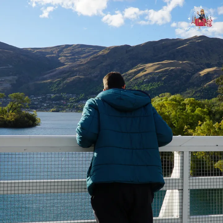 A man in a teal jacket seen from behind, taking in the view of Lake Wakatipu from the bridge