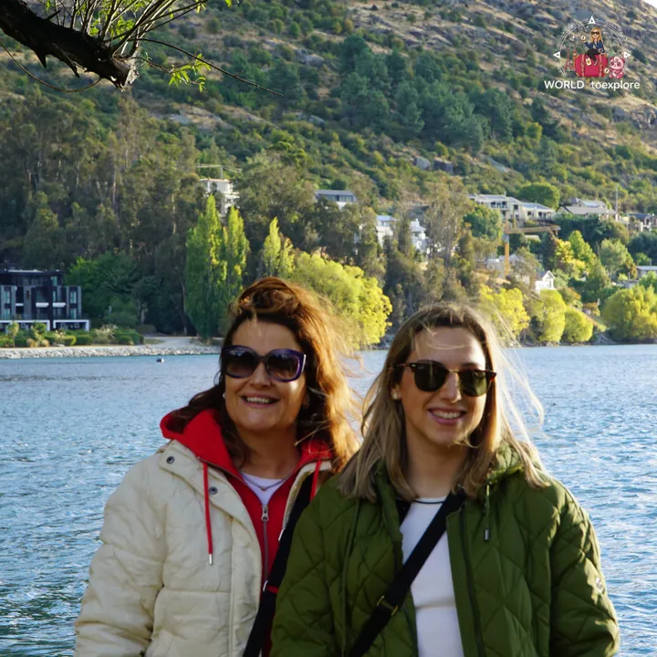The author and her mother smiling by Lake Wakatipu, with houses on the hillside in the background