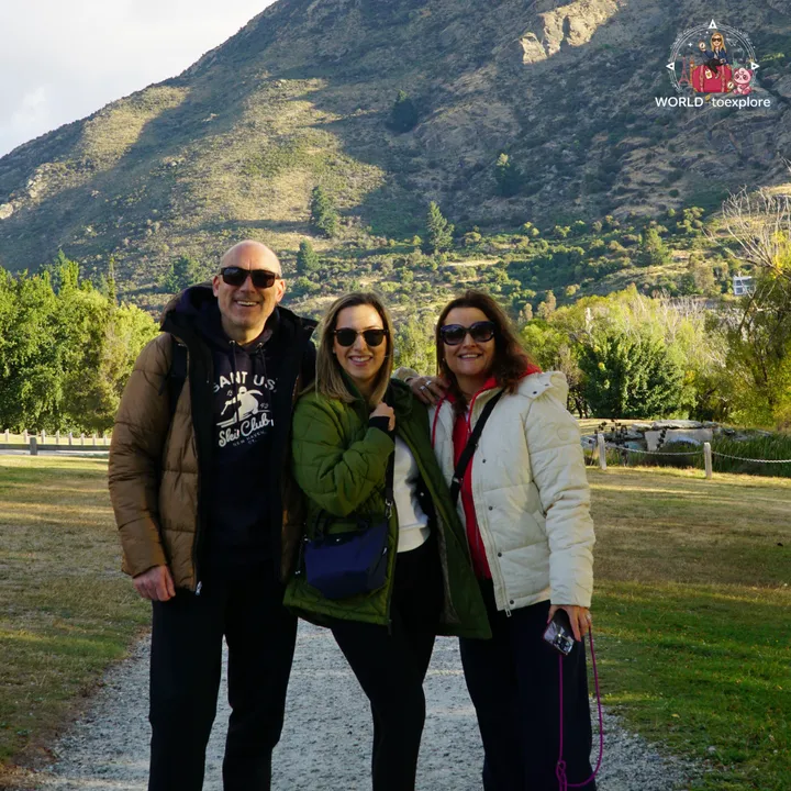 A group of three people smiling in the Peace Park Wakatipu Reforestation Trust, with the Queenstown mountains in the background