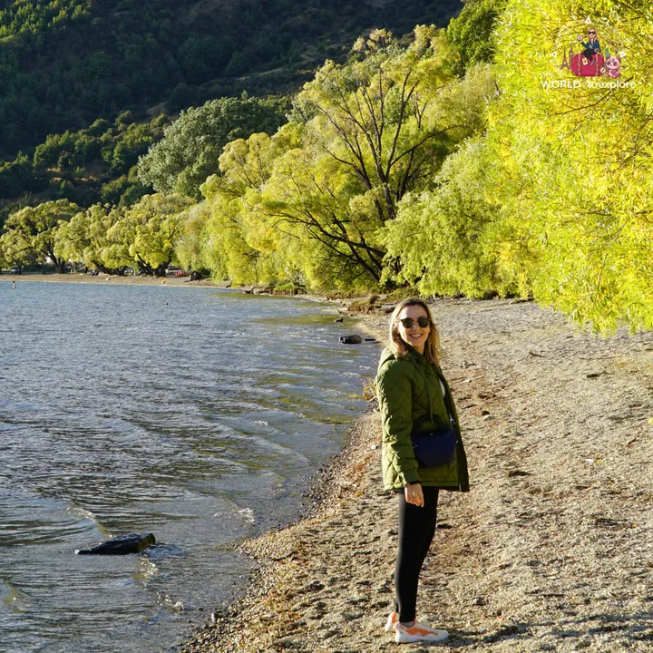 The author smiling on the shore of Frankton Beach, with yellow autumn trees and Lake Wakatipu in the background