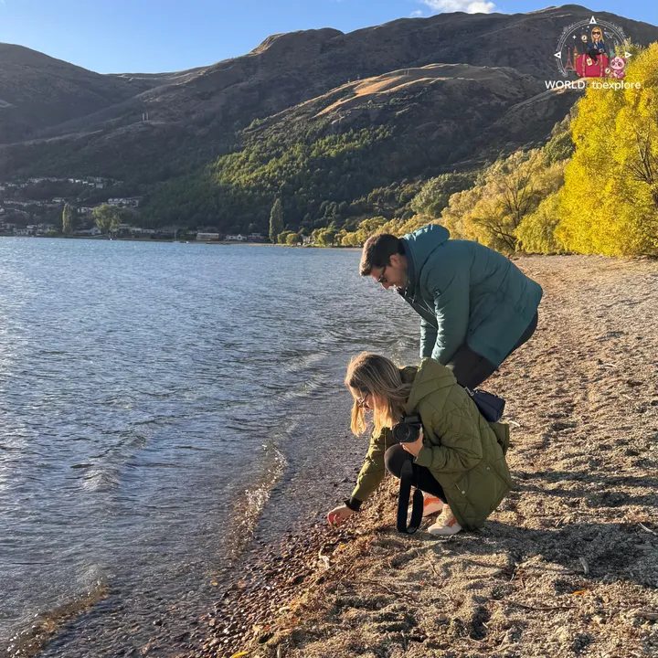 A couple crouching by the water at Frankton Beach, picking up stones on the shore of Lake Wakatipu