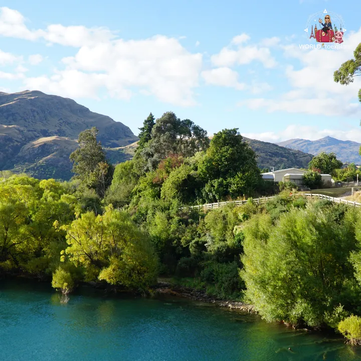 Turquoise-green waters of Lake Wakatipu by the shore, with trees and a wooden fence