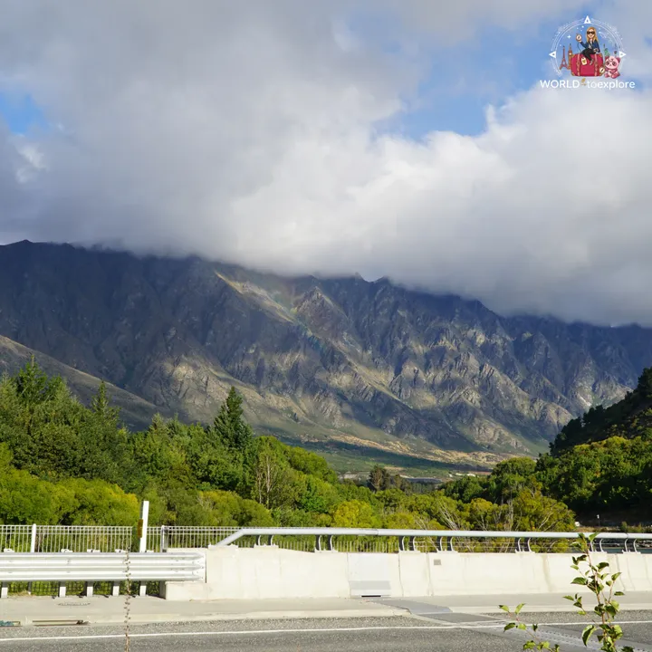 View of the Queenstown mountains with a rainbow forming through the clouds, next to the Kawarau Falls Dam