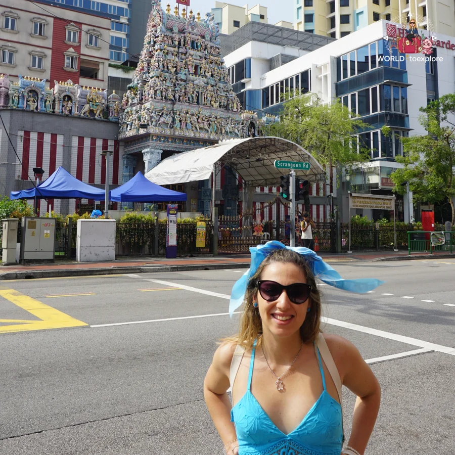 Cristina in a blue dress and bow in her hair, with the Sri Veeramakaliamman Hindu temple and its tower of colourful sculptures behind her, on Serangoon Road