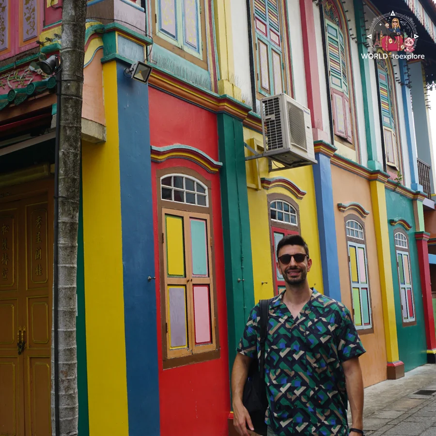Her husband beside a colourful façade with yellow, red, blue and green windows, in Little India