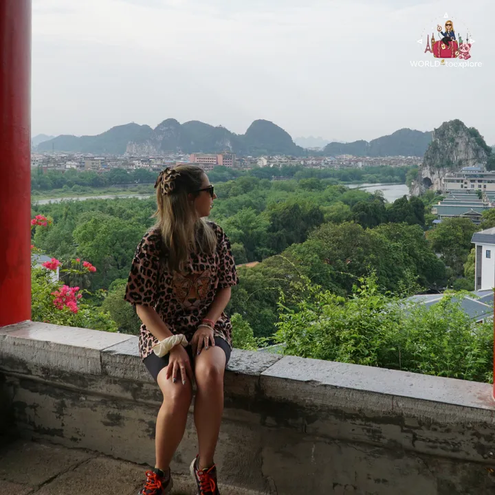 Cristina sitting at a viewpoint with red columns, with the Li River and Guilin's karst mountains in the background