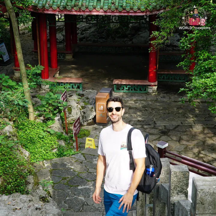Man smiling next to a traditional Chinese pavilion, with a green roof and red columns