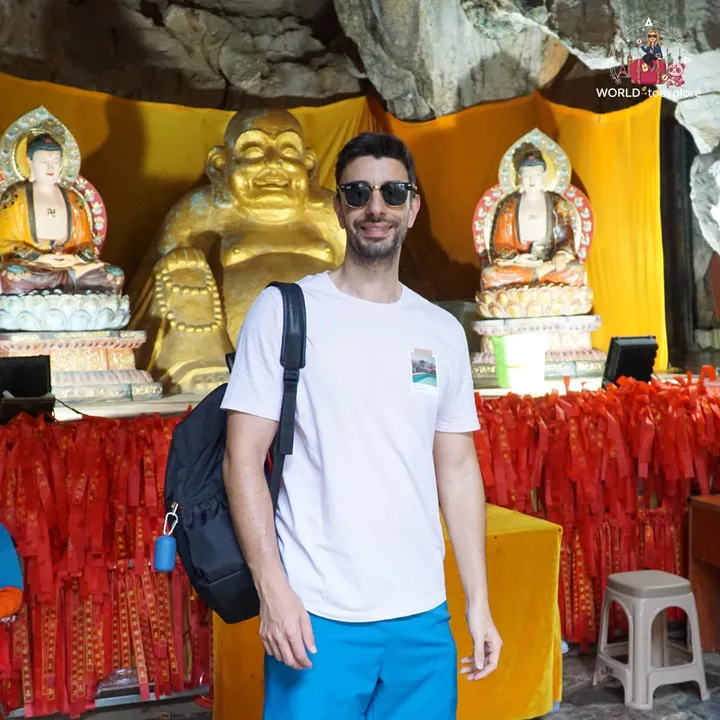 Man smiling next to golden Buddha statues, inside Wind Cave