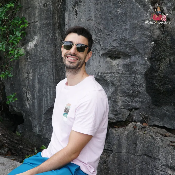 Man smiling, leaning against the rock, next to a natural mark that looks like a face